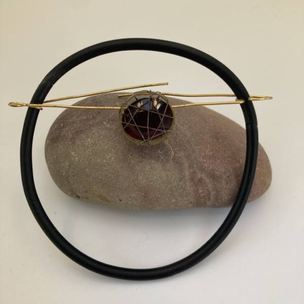 Brooch, mixed materials, exploring experimental setting techniques- circular rubber ring held by brass wire to create brooch pin, faceted ruby coloured glass stone balanced with wire wrapping in center.