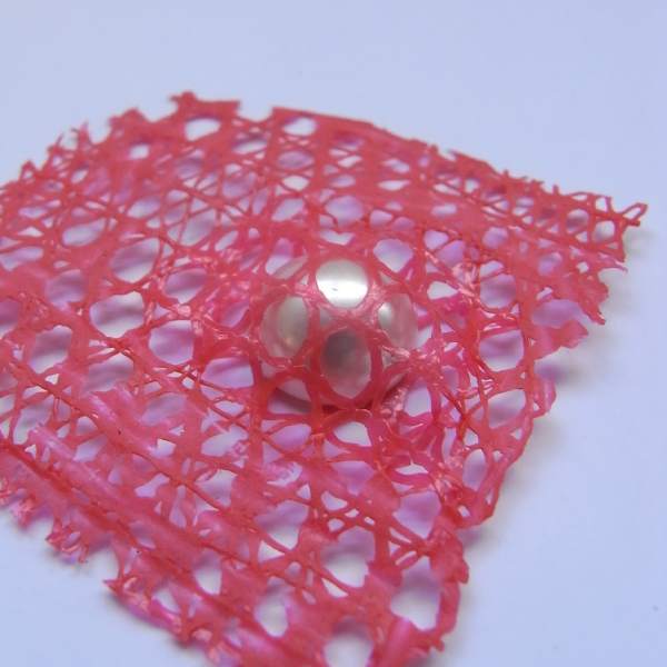 Experimental jewellery - stone setting using pearl bead, heat fused inside red plastic fruit netting